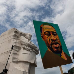 A demonstrator wearing a protective mask holds a painting of George Floyd at Martin Luther King Jr. memorial during the "Get Your Knee Off Our Necks" March on Washington in Washington